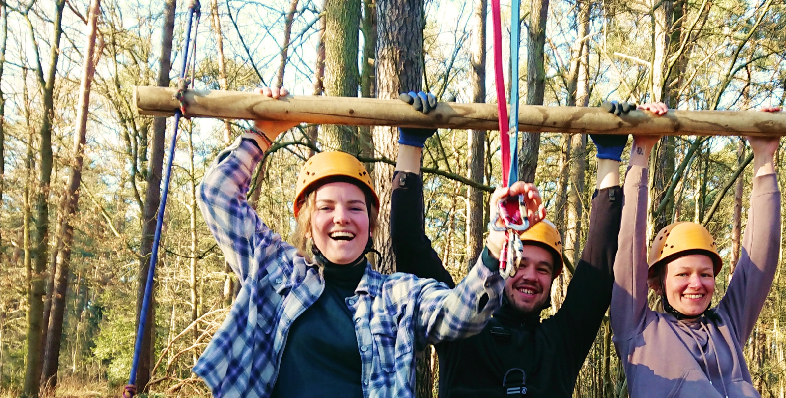 Drei Jugendliche im Halbportrt mit erhobenen Armen hngen an einem Balken un schauen lachend in die Kamera