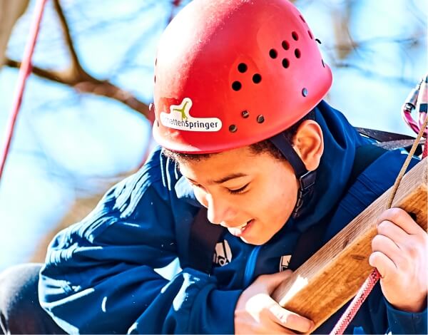 Kind klettert mit Helm gesichert an einem Gerst
