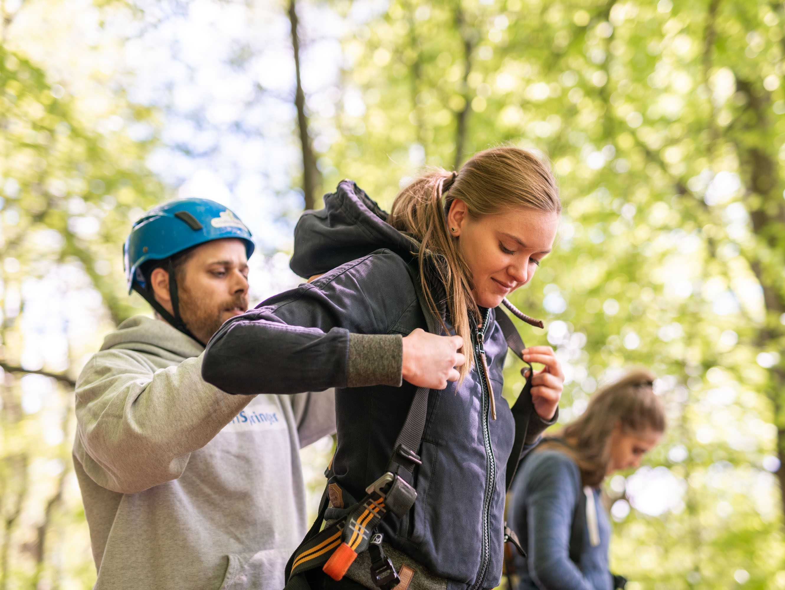 Mitarbeiter hilft einer Jugendlichen beim anlegen des Klettergurtes